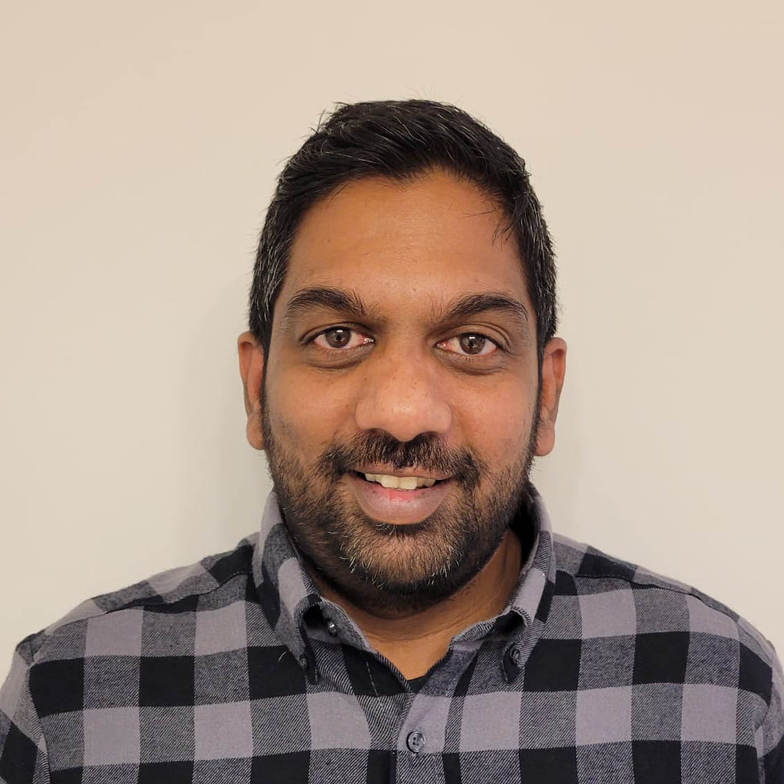 A headshot of Roshan Peiris, a Sri Lankan man wearing a black and gray checkered shirt in a white background.