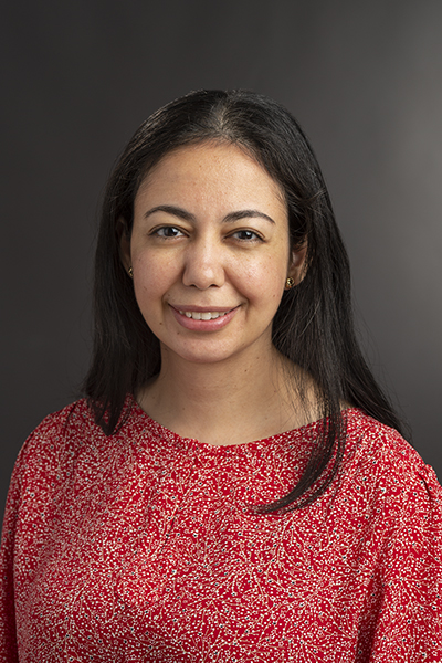 A headshot of Yasmine Elglaly. She is wearing a red patterned blouse and is posed against a dark gray background.