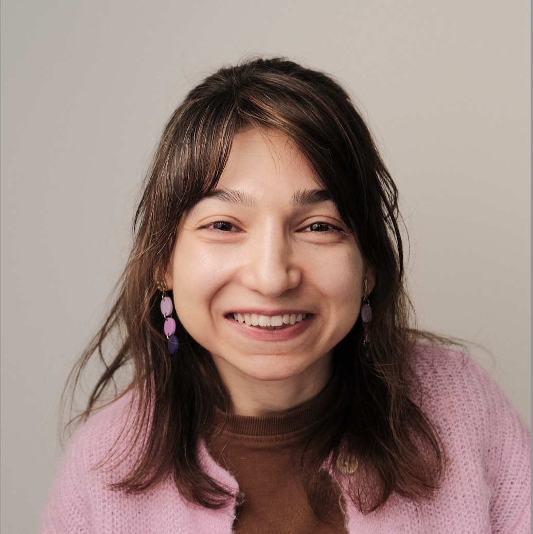 A picture of Zeynep Yıldız, a smiling woman with brown hair and brown eyes, wearing a pink cardigan.
